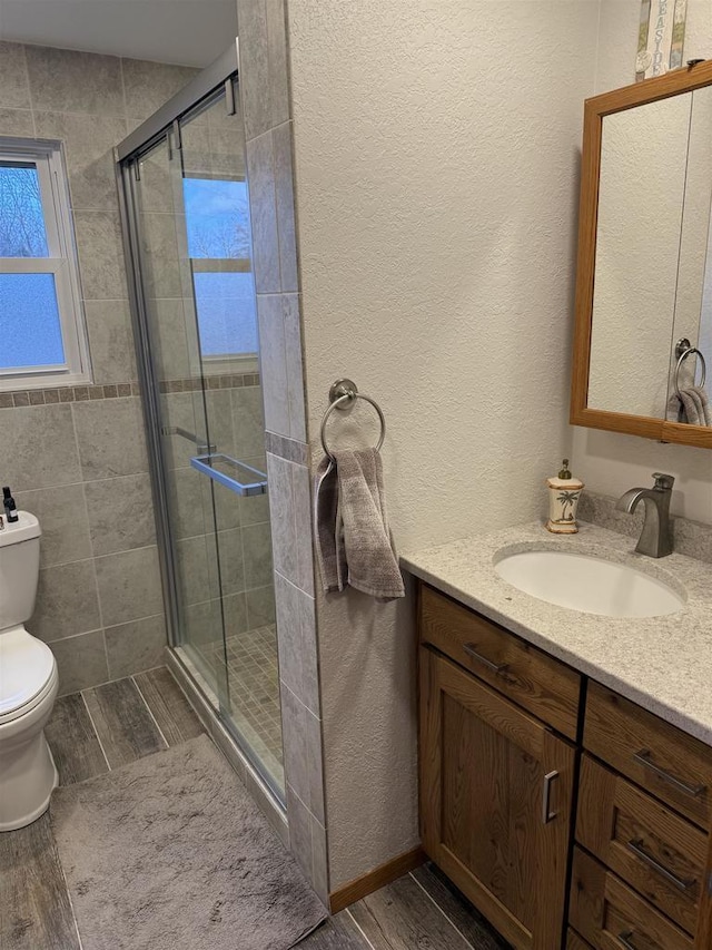 bathroom with a stall shower, vanity, toilet, and wood finished floors