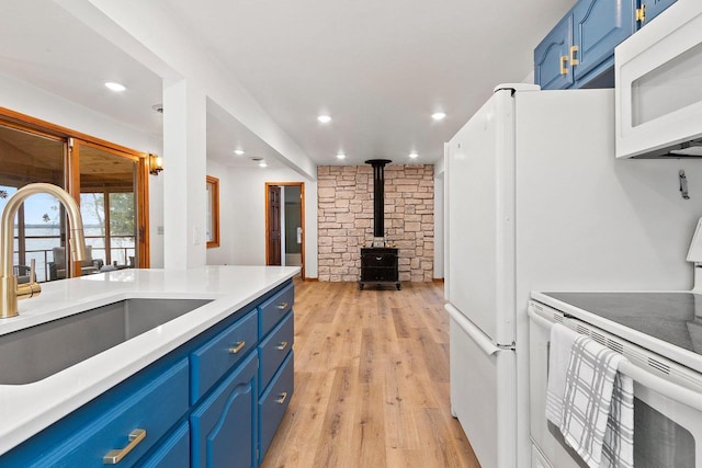 kitchen featuring white appliances, a sink, light wood-style floors, blue cabinetry, and a wood stove