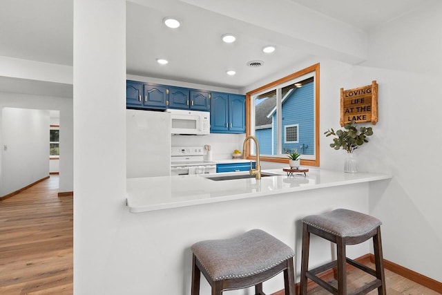 kitchen with blue cabinets, white appliances, wood finished floors, a sink, and a kitchen breakfast bar