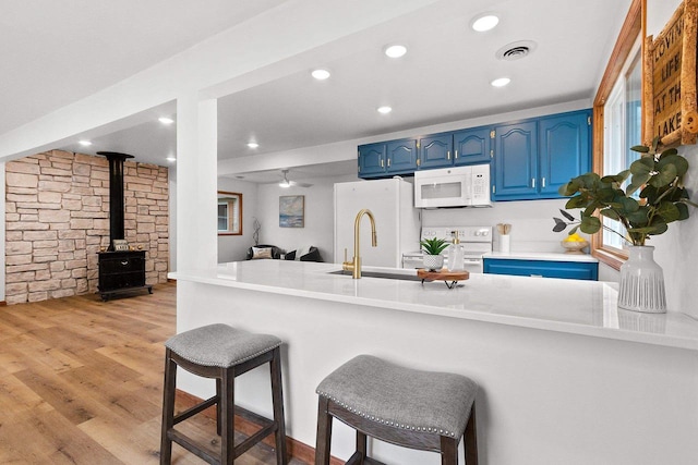 kitchen featuring light wood-style floors, a wood stove, blue cabinets, white appliances, and a kitchen bar