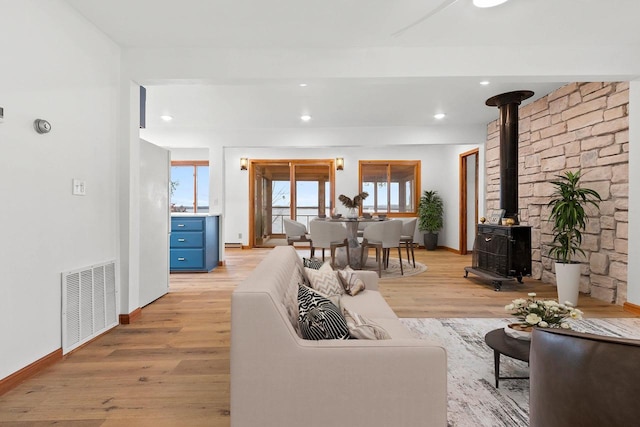 living area featuring recessed lighting, visible vents, baseboards, light wood-type flooring, and a wood stove