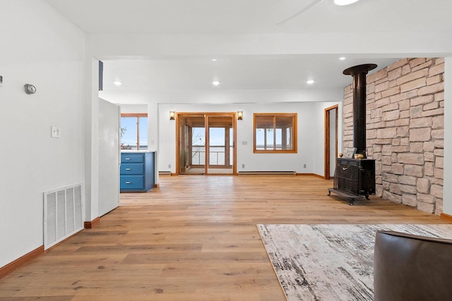 unfurnished living room featuring a wood stove, light wood finished floors, baseboard heating, and visible vents