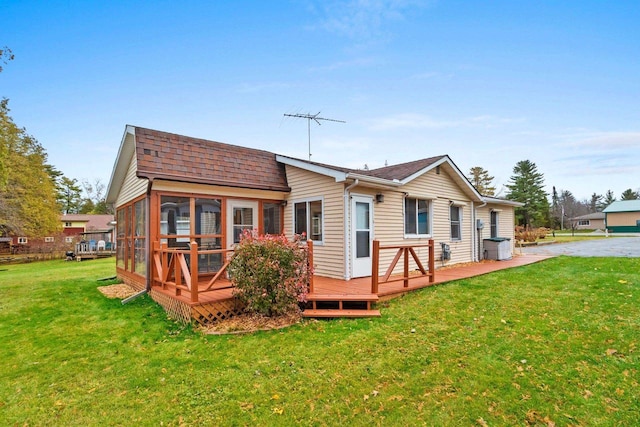 rear view of property featuring a sunroom, roof with shingles, a lawn, and a wooden deck