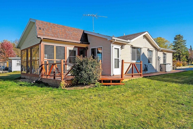 rear view of house with a deck, roof with shingles, a lawn, and a sunroom