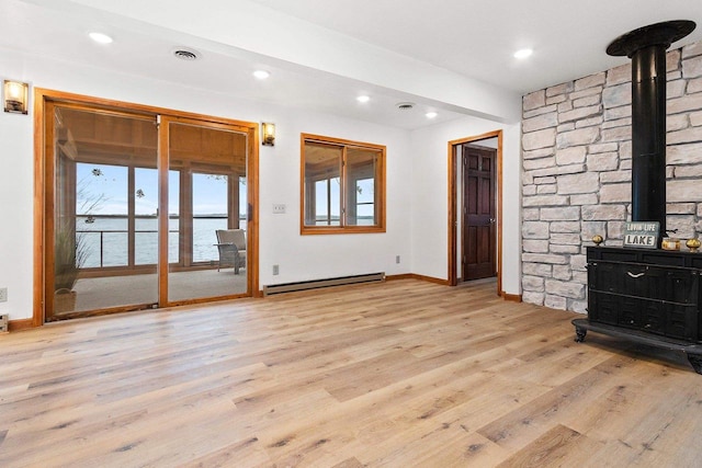 unfurnished living room featuring baseboards, wood finished floors, a wood stove, a water view, and a baseboard heating unit