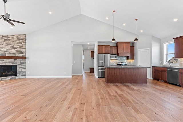 kitchen featuring light wood finished floors, a kitchen island, open floor plan, stainless steel appliances, and a fireplace