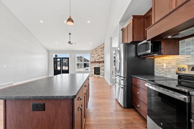 kitchen with light wood finished floors, dark countertops, appliances with stainless steel finishes, a center island, and custom exhaust hood