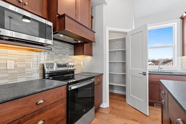 kitchen featuring a sink, appliances with stainless steel finishes, decorative backsplash, light wood finished floors, and dark countertops