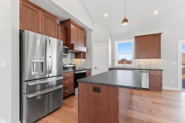 kitchen with appliances with stainless steel finishes, dark countertops, a center island, and under cabinet range hood