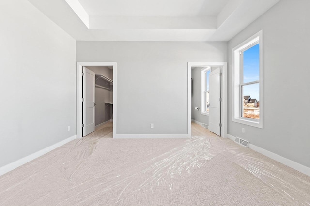 unfurnished bedroom with a tray ceiling, visible vents, and baseboards