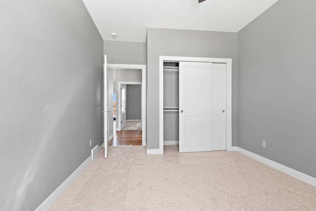 unfurnished bedroom with a closet, light colored carpet, visible vents, and baseboards