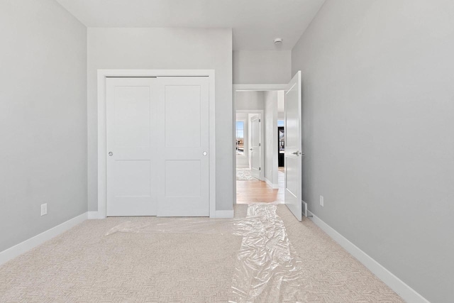 unfurnished bedroom featuring a closet, light colored carpet, and baseboards