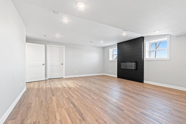 interior space featuring a large fireplace, light wood-type flooring, and baseboards