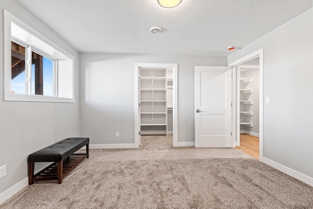 unfurnished bedroom with carpet floors, a walk in closet, and baseboards