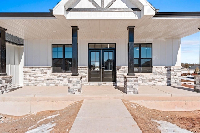 property entrance featuring board and batten siding, stone siding, a porch, and french doors