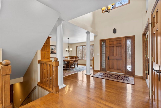 entrance foyer with ornate columns, a notable chandelier, baseboards, and wood finished floors