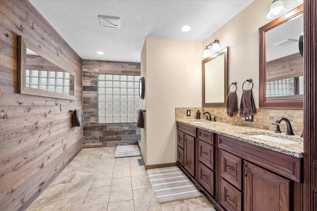 bathroom with tiled shower, a sink, a textured ceiling, and decorative backsplash