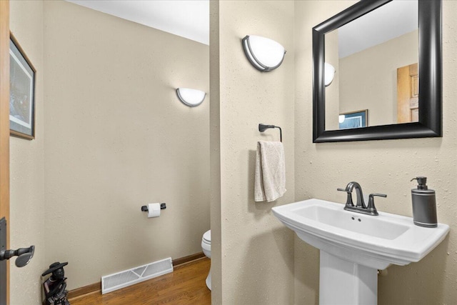 bathroom with visible vents, toilet, a sink, wood finished floors, and baseboards