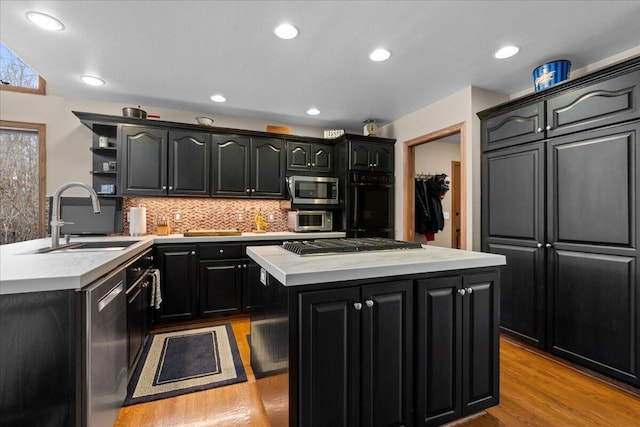 kitchen featuring a kitchen island, dark cabinets, stainless steel appliances, light countertops, and a sink