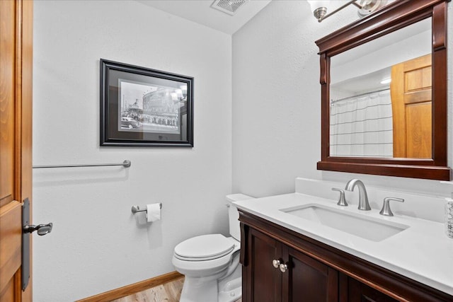 bathroom with toilet, wood finished floors, vanity, visible vents, and baseboards