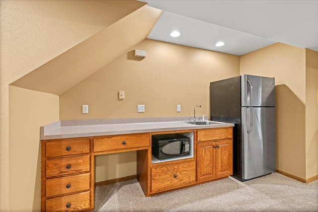 kitchen featuring black microwave, light carpet, a sink, freestanding refrigerator, and brown cabinetry