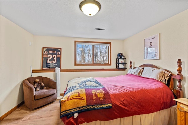 bedroom featuring visible vents, a textured ceiling, baseboards, and wood finished floors