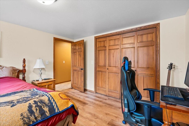 bedroom featuring light wood-style flooring, a textured ceiling, baseboards, and a closet