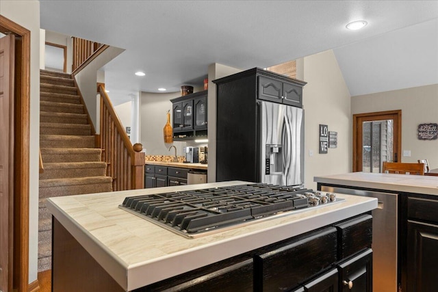 kitchen featuring stainless steel appliances, recessed lighting, glass insert cabinets, vaulted ceiling, and dark cabinetry