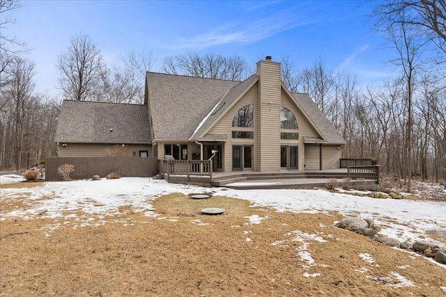 snow covered back of property with a chimney and a wooden deck