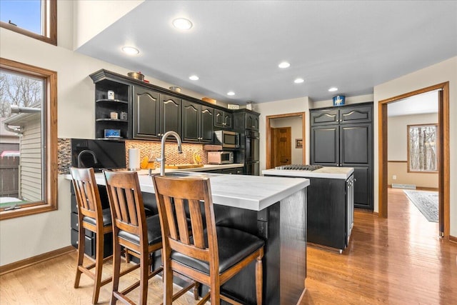 kitchen featuring a kitchen island, stainless steel microwave, a peninsula, open shelves, and a sink