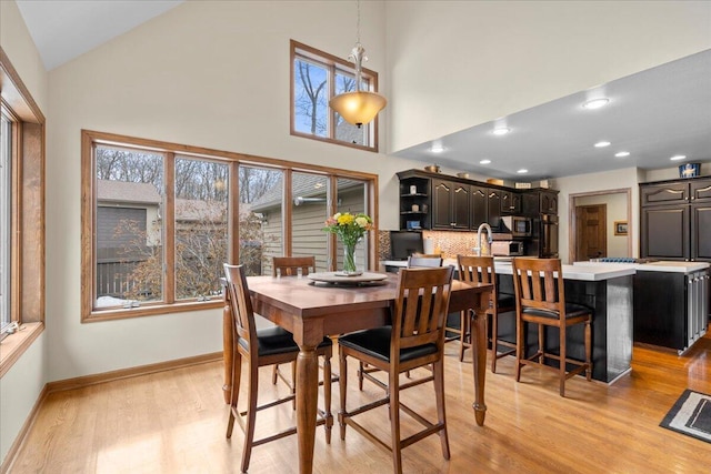 dining room with light wood-style floors, recessed lighting, high vaulted ceiling, and baseboards