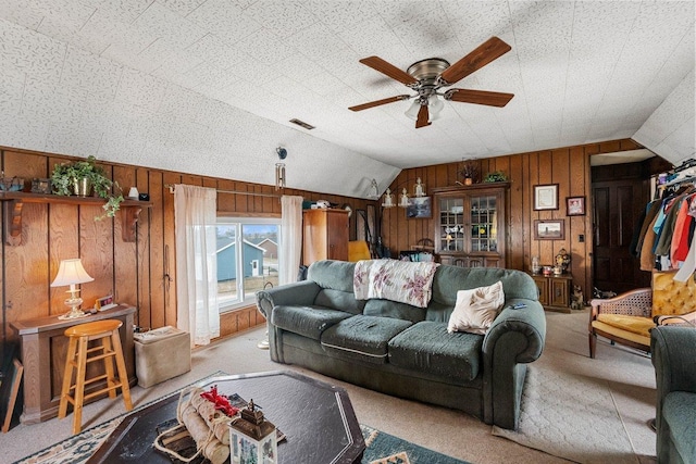 carpeted living room featuring lofted ceiling, wooden walls, visible vents, and a ceiling fan