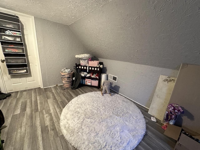 interior space featuring visible vents, a textured wall, lofted ceiling, wood finished floors, and a textured ceiling