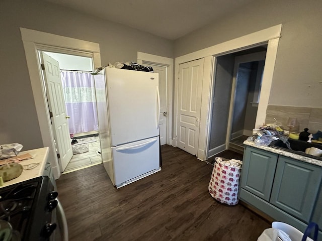 kitchen featuring gas stove, light countertops, dark wood-style flooring, and freestanding refrigerator