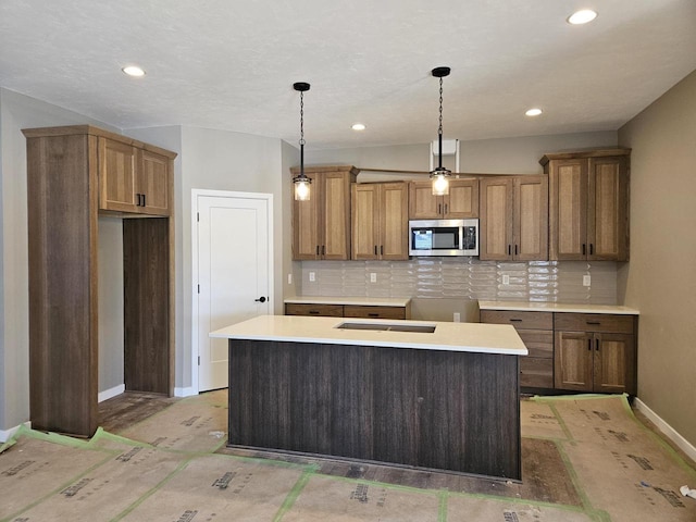 kitchen with baseboards, brown cabinets, tasteful backsplash, stainless steel microwave, and pendant lighting