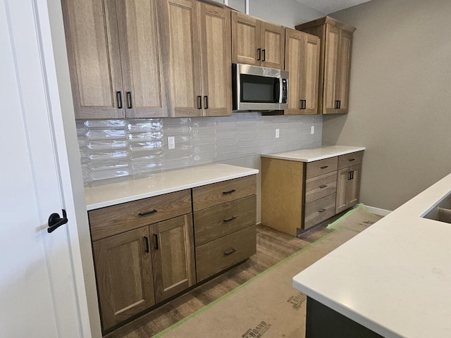 kitchen with brown cabinets, light countertops, stainless steel microwave, backsplash, and wood finished floors