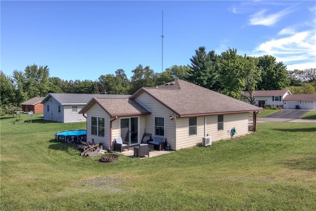 rear view of property featuring ac unit, a yard, a patio, a shingled roof, and an outdoor fire pit