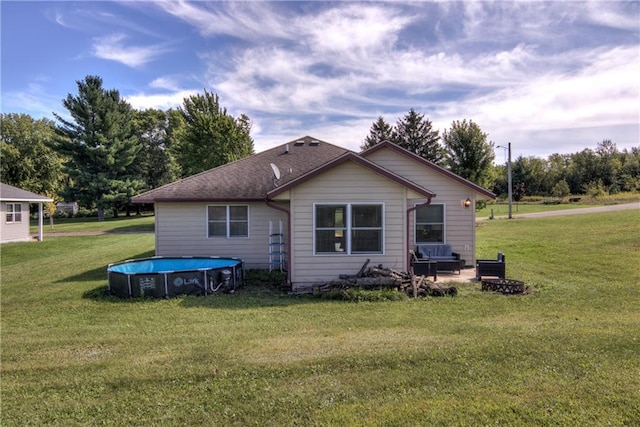 rear view of property featuring a shingled roof, an outdoor pool, and a lawn