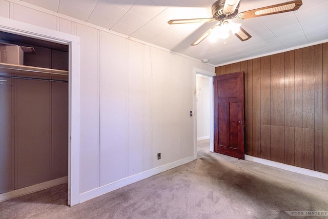 unfurnished bedroom featuring a closet, a decorative wall, ornamental molding, carpet flooring, and ceiling fan