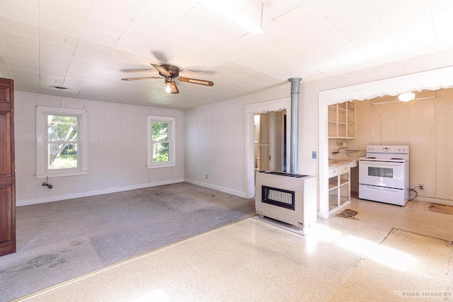 unfurnished living room with baseboards, ceiling fan, a wood stove, and heating unit