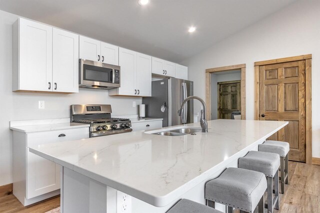 N8791 Lake Cabin Dr, New Lisbon, WI 53950 - kitchen with stainless steel appliances, a kitchen island with sink, vaulted ceiling, a sink, and white cabinetry