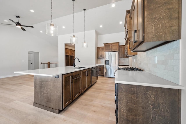 kitchen featuring a sink, light wood-style flooring, stainless steel fridge, and a center island with sink