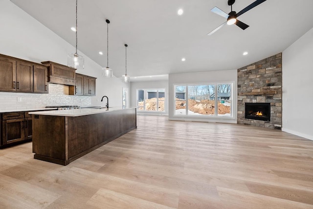 kitchen featuring light wood-style floors, a ceiling fan, dark brown cabinetry, a sink, and an island with sink