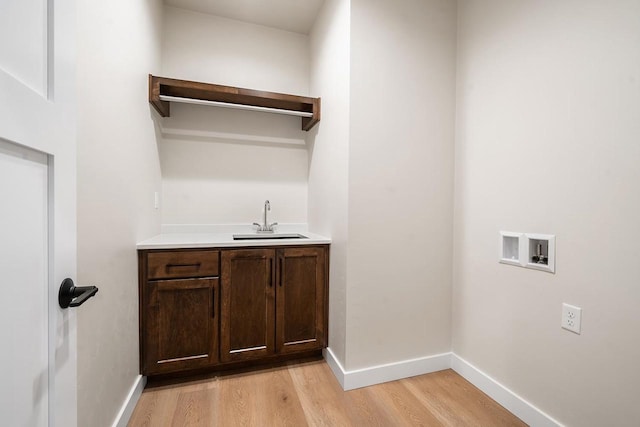 laundry room with hookup for a washing machine, a sink, baseboards, light wood-type flooring, and cabinet space