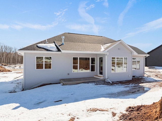 snow covered property with roof with shingles