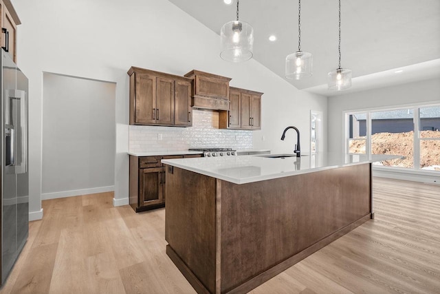 kitchen featuring high end refrigerator, range, light countertops, light wood-style floors, and a sink