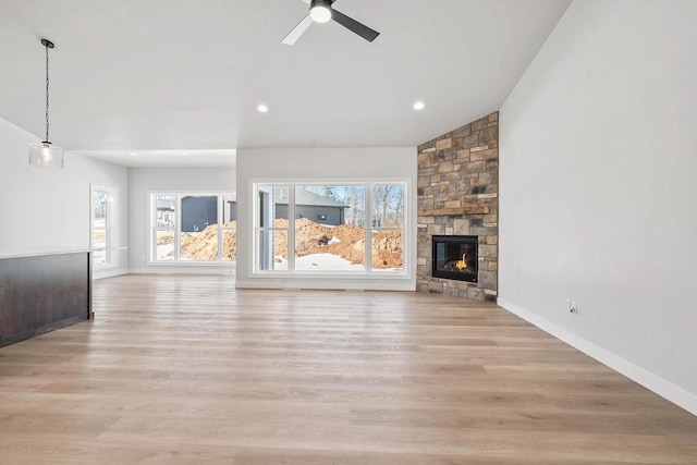 unfurnished living room featuring lofted ceiling, light wood-style flooring, a ceiling fan, and a stone fireplace