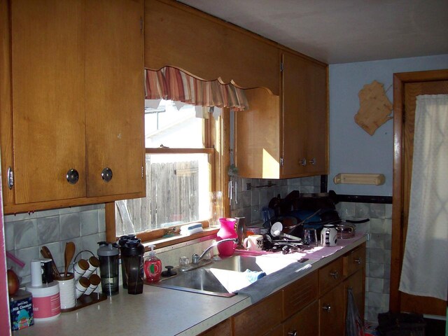 1002 Adams St, Portage, WI 53901 - kitchen with decorative backsplash, brown cabinets, a sink, and light countertops