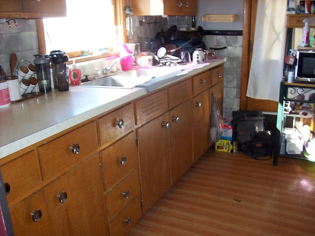 1002 Adams St, Portage, WI 53901 - kitchen with light countertops, light wood-type flooring, brown cabinets, a sink, and decorative backsplash