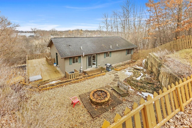 rear view of house with a fire pit, a deck, a shingled roof, and fence